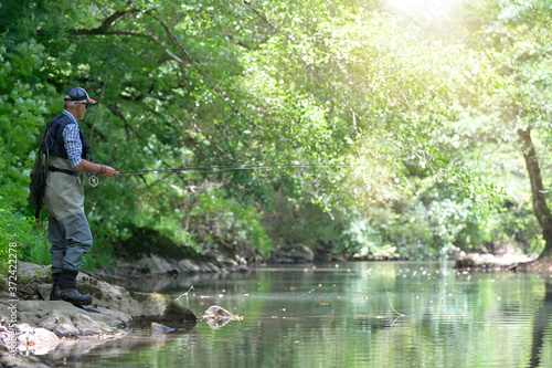 fly fisherman in summer fishing in a mountain river with waders and a cap © goodluz