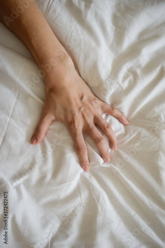 Close up sexy woman hand pulling and squeezing white sheets in ecstasy in bed. Orgasm on white bed. Sex and erotic concept.