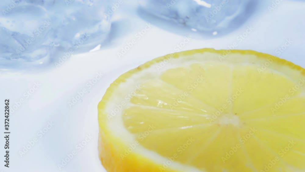 Close up shot of a delicious yellow lemon slice. Camera moving down with melting ice cubes on a light blue and white table. Close up shot of a delicious yellow lemon slice. Camera moving down with melting ice cubes on a light blue and white table.