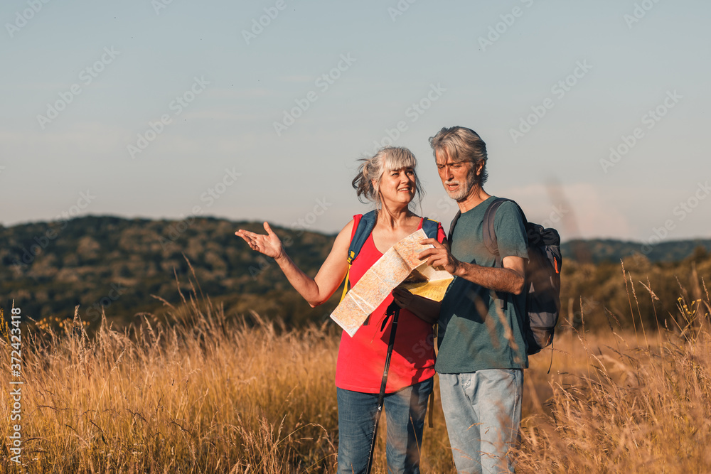 Active senior couple hiking in nature with backpacks, enjoying their adventure at sunset.