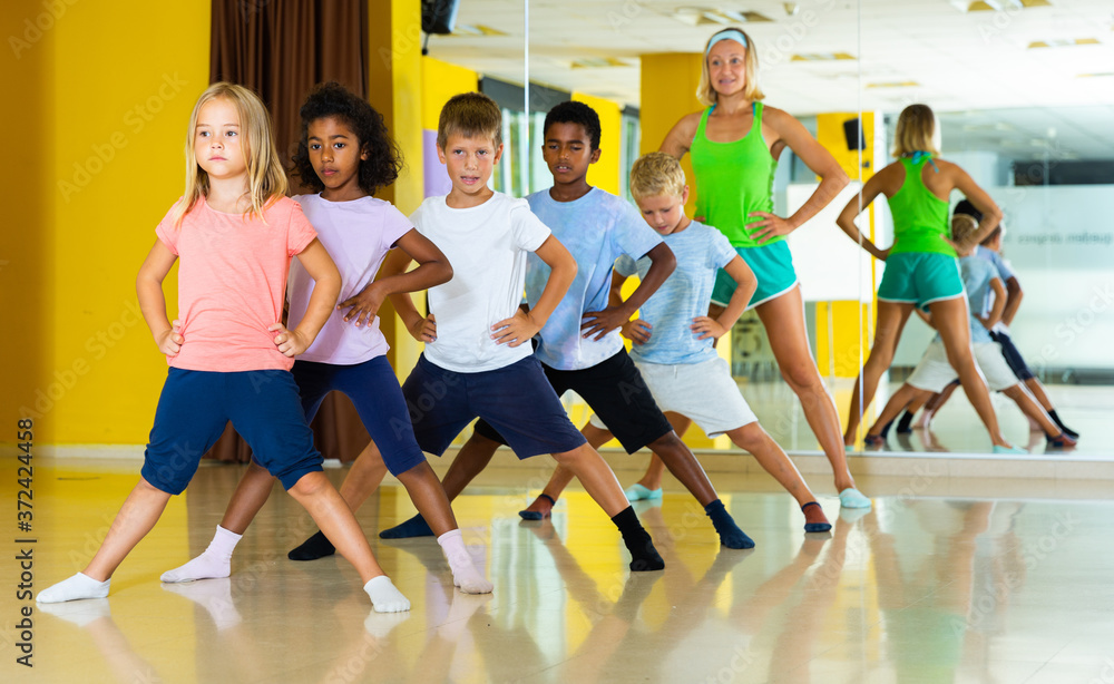Children dancing synchronous group choreography with female coach in dance hall.