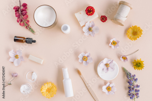White containers of beauty treatments, aromatherapy oil, organic soaps, eco friendly toothbrush, flower buds on beige background.