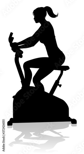 A woman in silhouette using a stationary exercise spin bike piece of gym equipment fitness machine