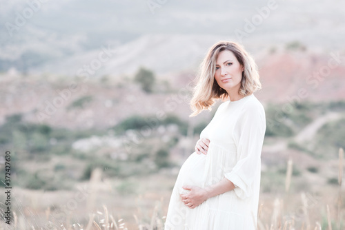 Pregnant woman wearing dress posing outdoors over nature background. Motherhood. Maternity. Healthy lifestyle. Happiness.