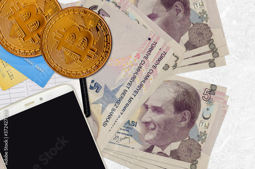 5 Turkish lira bills and golden bitcoins with smartphone and credit cards. Cryptocurrency investment concept. Crypto mining or trading photo