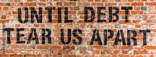 A background of a brick wall with the text "Until Debt tear us apart" painted on it. It is a text referencing to the European financial crisis