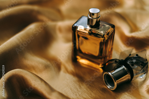 Perfume bottle on golden satin fabric, close-up, warm light. 