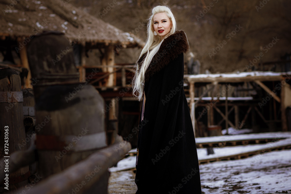 Beautiful blonde Viking dressed in a black cloak against the backdrop of the castle Beautiful blonde Viking dressed in a black cloak against the backdrop of the castle