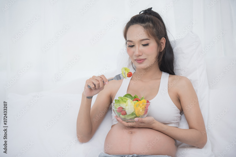 care about unborn child. pregnancy, healthy food and people concept, happy pregnant woman eating vegetable salad for breakfast sitting on bed at home. pregnancy and healthy organic nutrition. care about unborn child. pregnancy, healthy food and people concept, happy pregnant woman eating vegetable salad for breakfast sitting on bed at home. pregnancy and healthy organic nutrition.