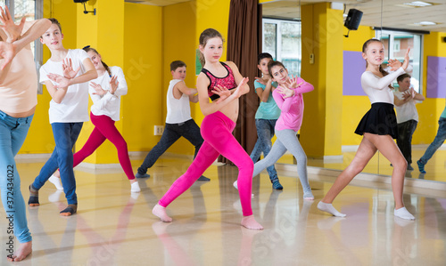 Teenage boys and girls practicing dance, stretching with female trainer in dance hall
