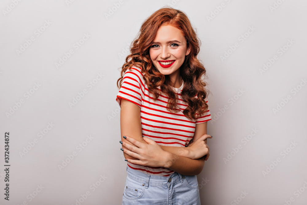 Adorable slim lady in striped t-shirt smiling to camera. Appealing red-haired girl having fun in studio. Adorable slim lady in striped t-shirt smiling to camera. Appealing red-haired girl having fun in studio.