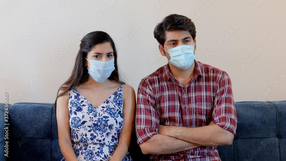 Young boyfriend girlfriend using protective medical masks while sitting at home. Sick Indian couple talking to each other with folded hands while wearing surgical masks during Covid-19 pandemic Young boyfriend girlfriend using protective medical masks while sitting at home. Sick Indian couple talking to each other with folded hands while wearing surgical masks during Covid-19 pandemic