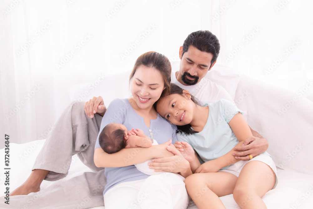 Happy family concept, father and daughter sit on bed excited looking new member in family, adorable newborn sleep on mother chest, mom hold infant embracing and caring while look daughter with love Happy family concept, father and daughter sit on bed excited looking new member in family, adorable newborn sleep on mother chest, mom hold infant embracing and caring while look daughter with love