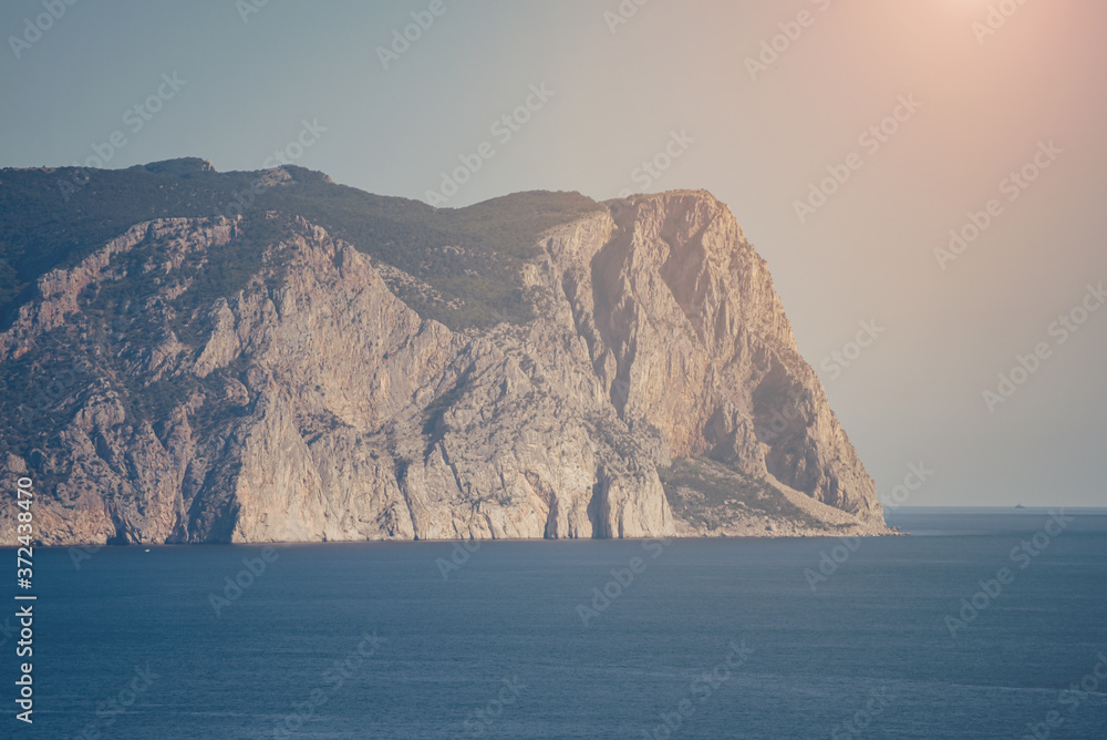 Colorful landscape with blue sea, mountain and sky with sun in the evening. Mountain covered with trees. Seascape