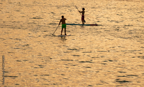 Recreation on the sea.  During hot summer weather two people maneuver their paddle boards across the golden hour water as the sun begins to set.