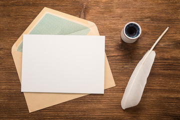 Envelope, goose feather, inkwell on a wood table  