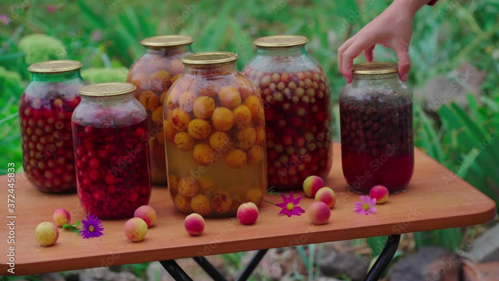 Jars with kompot on table. Sealed glass jars with kompot placed on table near flowers and fruits on summer day in garden Jars with kompot on table. Sealed glass jars with kompot placed on table near flowers and fruits on summer day in garden