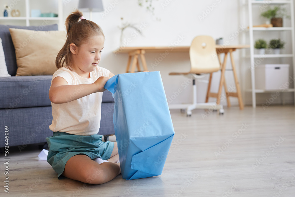 Little girl opening the big present while sitting on the floor in the room Little girl opening the big present while sitting on the floor in the room