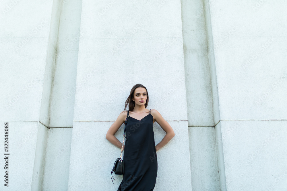 Outdoors fashion portrait of trendy pretty girl posing on the white wall in the city.