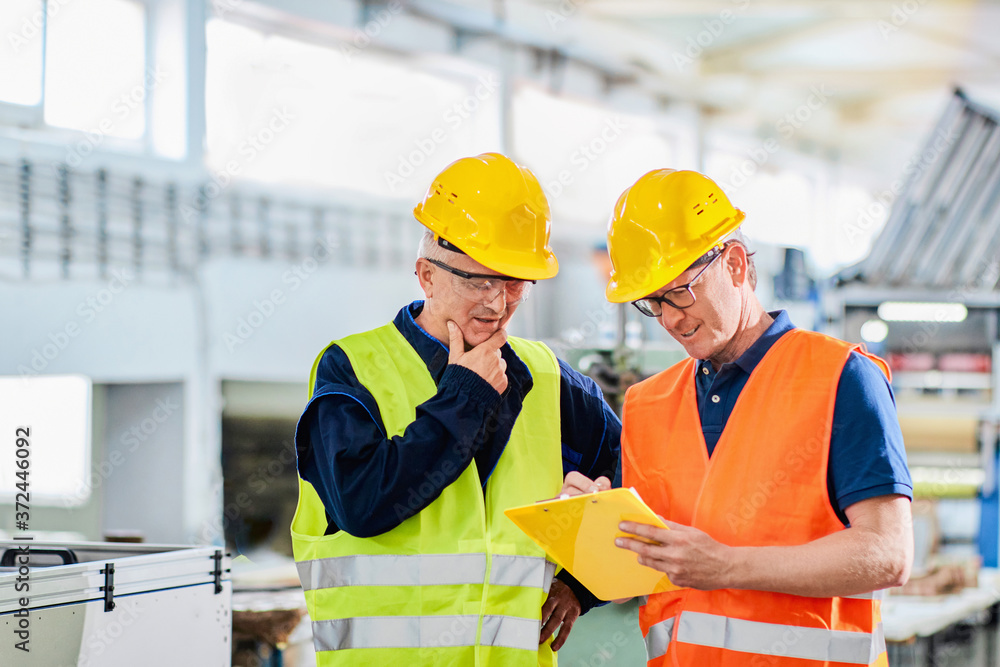 An engineer and a manager working together in a factory, wearing protective wear
An engineer and a manager working together in a factory, wearing protective wear
