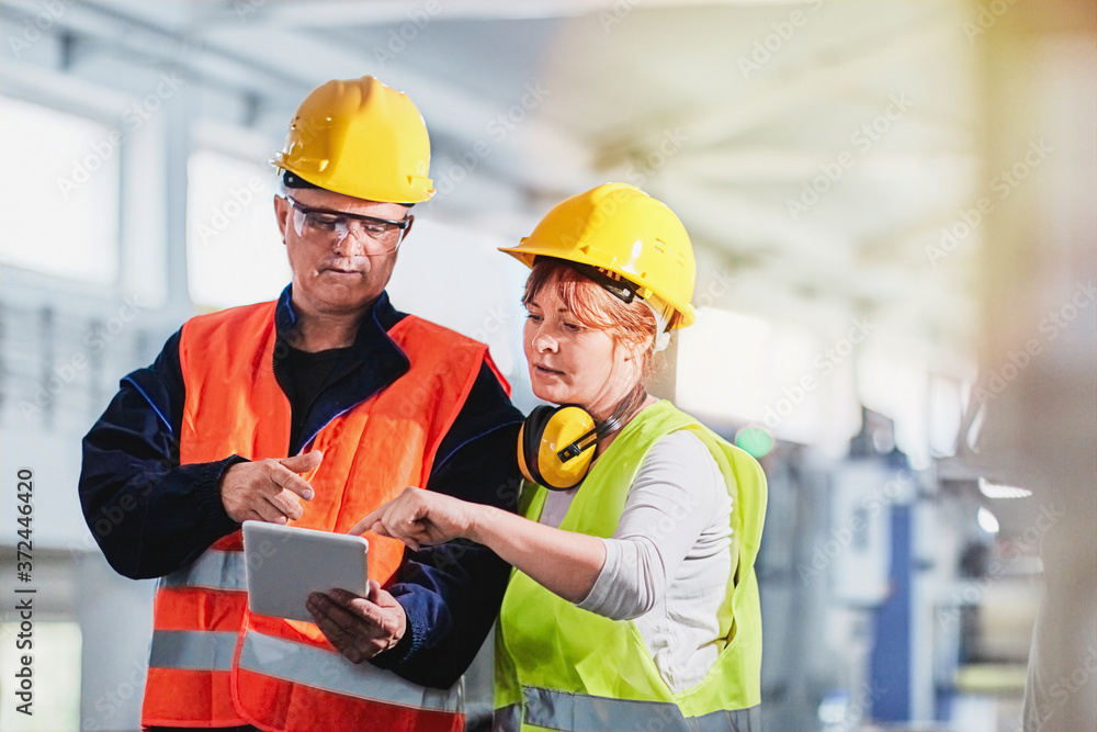 An engineer and a manager working together in a factory, wearing protective wear An engineer and a manager working together in a factory, wearing protective wear