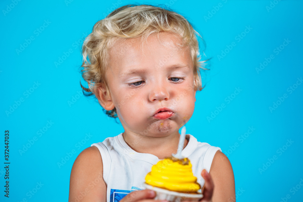 Lovely 1-year-old male baby with blue eyes with dirty face tries to blow out a lit candle on a yellow muffin. Horizontal. Lovely 1-year-old male baby with blue eyes with dirty face tries to blow out a lit candle on a yellow muffin. Horizontal.