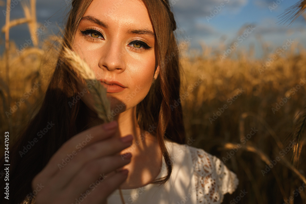 Smiling woman standing with wheat spikelet in field and looking at camera while enjoying summer holiday in countryside Smiling woman standing with wheat spikelet in field and looking at camera while enjoying summer holiday in countryside