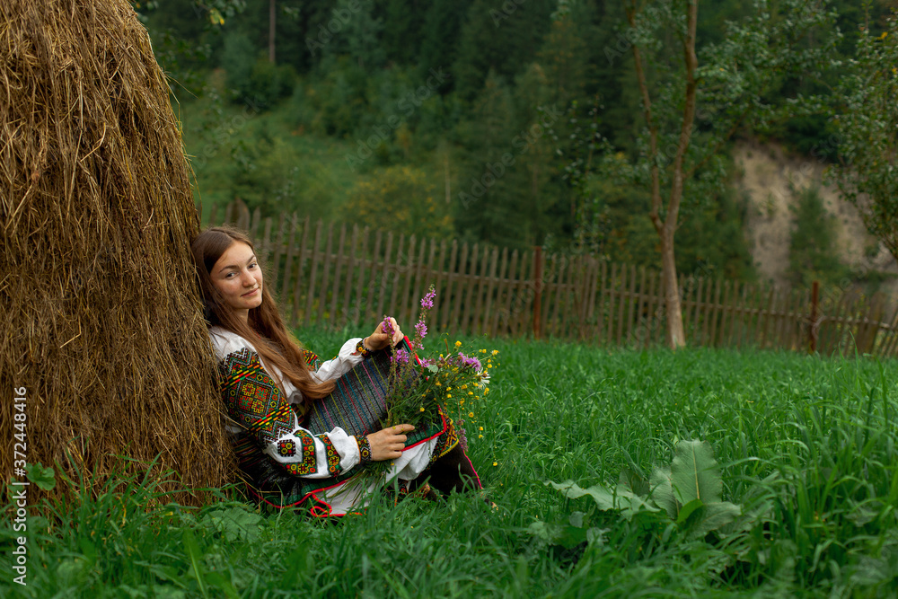 Fototapeta premium girl with loose hair with a bouquet of wildflowers sits on the grass