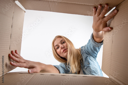 Young beautiful girl blonde, opens and peeks into a cardboard box. To get or to put things to move, bottom view.