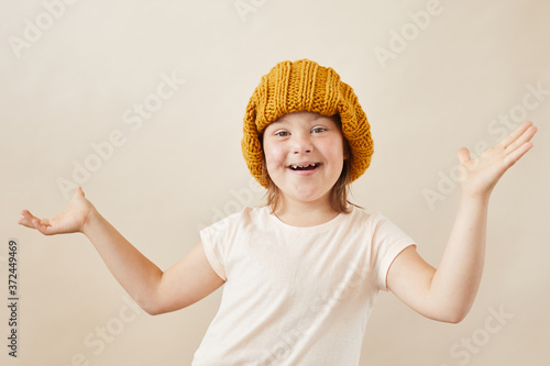 Fototapeta Portrait of happy girl with down syndrome wearing warm hat smiling at camera aga