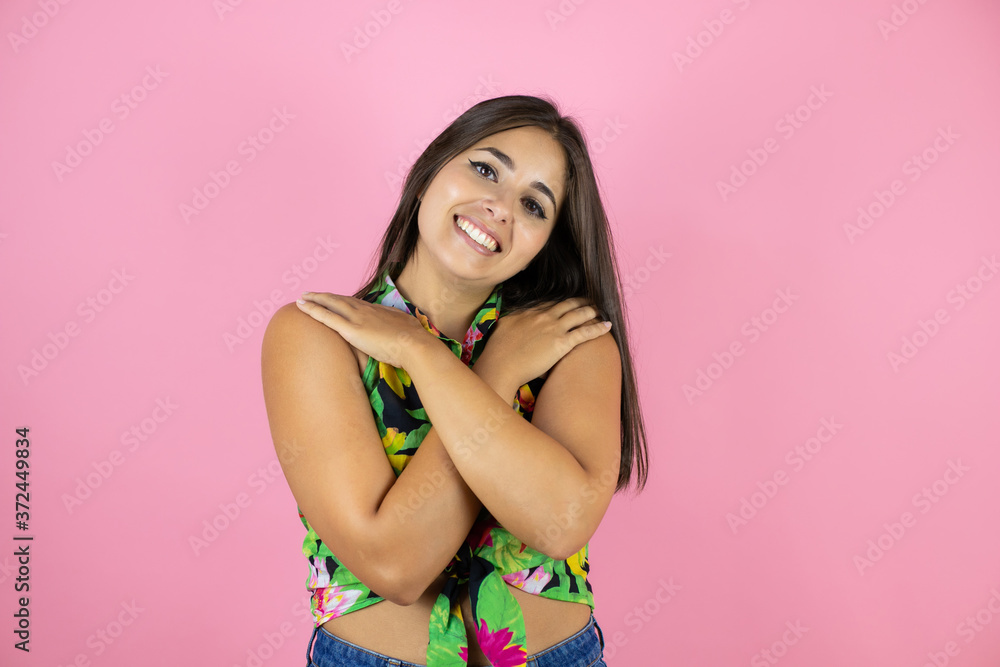Young beautiful woman standing over isolated pink background hugging oneself happy and positive, smiling confident