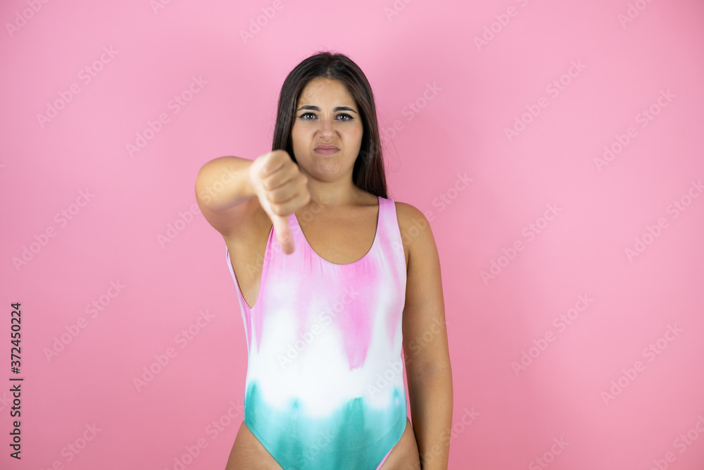 Young beautiful woman wearing swimsuit over isolated pink background with angry face, negative sign showing dislike with thumb down Young beautiful woman wearing swimsuit over isolated pink background with angry face, negative sign showing dislike with thumb down