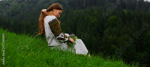 girl in embroidery with a bouquet of wild flowers sits in green grass