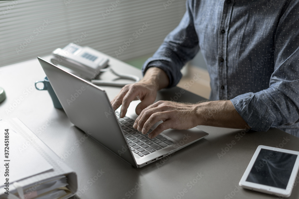 Businessman sitting at desk and typing on a laptop Businessman sitting at desk and typing on a laptop