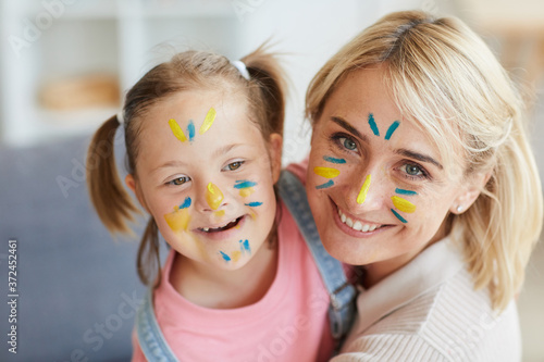 Portrait of happy mother and her daughter with down syndrome with painted faces smiling at camera