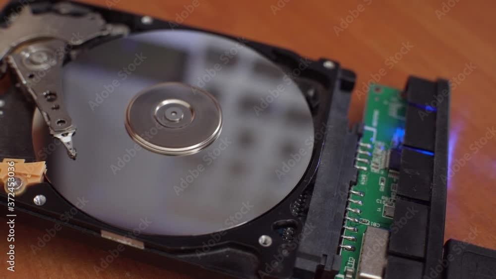 The hard disk is lying on the table, blinking and spinning the disk. Work of a hacked hard drive inside. Computer security. Internal structure of the hard disk. Lines of code and data flash in the bac The hard disk is lying on the table, blinking and spinning the disk. Work of a hacked hard drive inside. Computer security. Internal structure of the hard disk. Lines of code and data flash in the bac