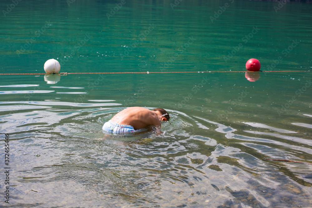 The boy examines the fish underwater. Mountain lake Mezzolla, Italy. Cold water in summer. Rest after quarantine.