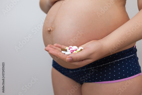 Pregnant woman holds pills in the palm of her hand against the background of her stomach