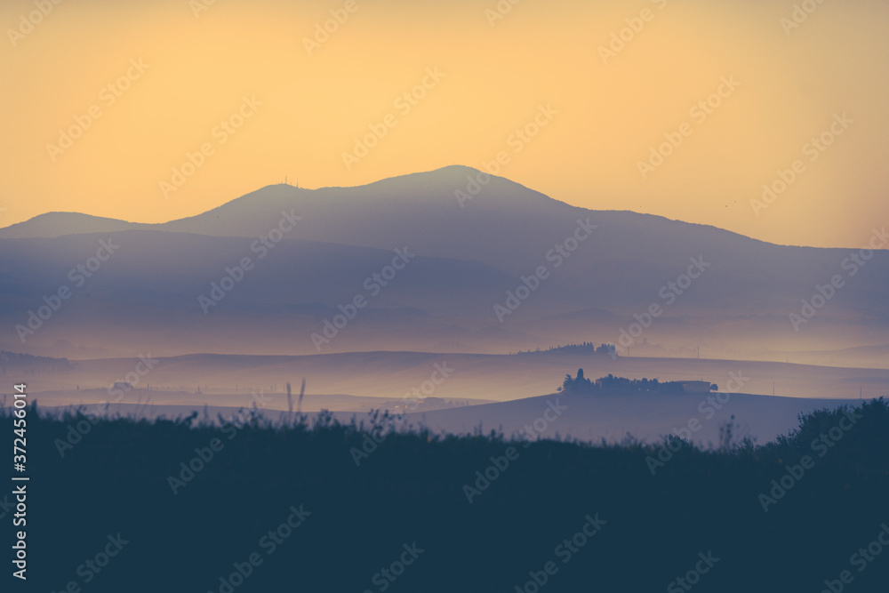 Obraz premium Tuscany morning landscape with mist, trees, old castle and mountains. Travel destination Tuscany. Monochrome