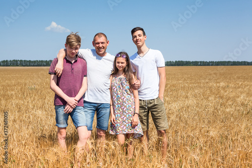 Single father with his teenage children, two sons and daughter. Cereal farmer family standing on wheat field, embracing and loving people