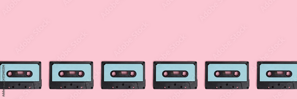 Fototapeta premium Row of cassette tapes on a pink pastel background. Creative banner with place for text.