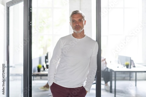 Happy businessman standing in the office with coworkers in the background working by the desk