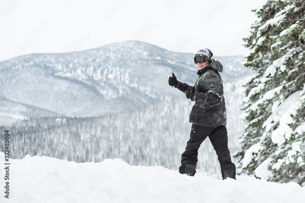 Snowboarder is standing on the winter slope and shows a thumbs up.