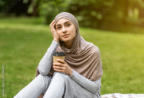 Dreamy arab girl sitting alone at park, drinking coffee