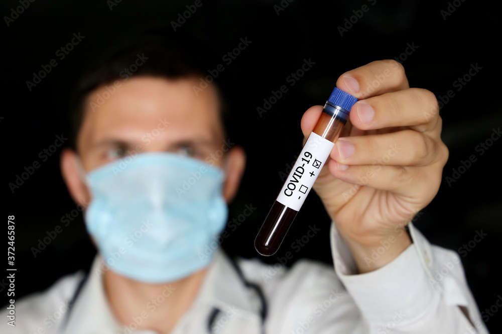 Test tube with covid-19 blood sample in male hand close up, man in medical mask holding a vial. Doctor or scientist with positive coronavirus test