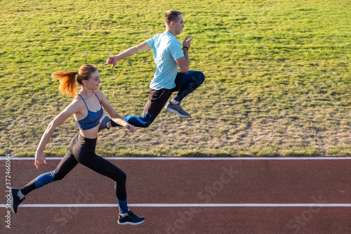Young couple of fit sportsmen boy and girl running while doing exercise on red tracks of public stadium outdoors. © bilanol