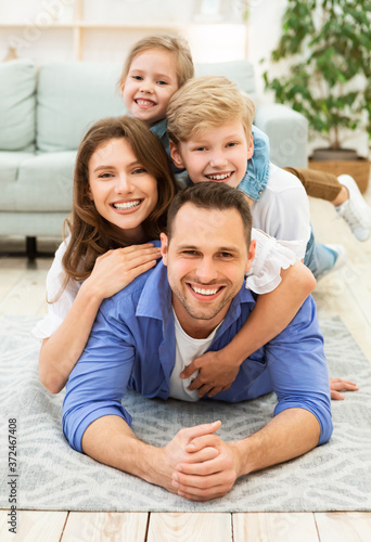 Positive Family Of Four Lying Posing On Floor Indoors