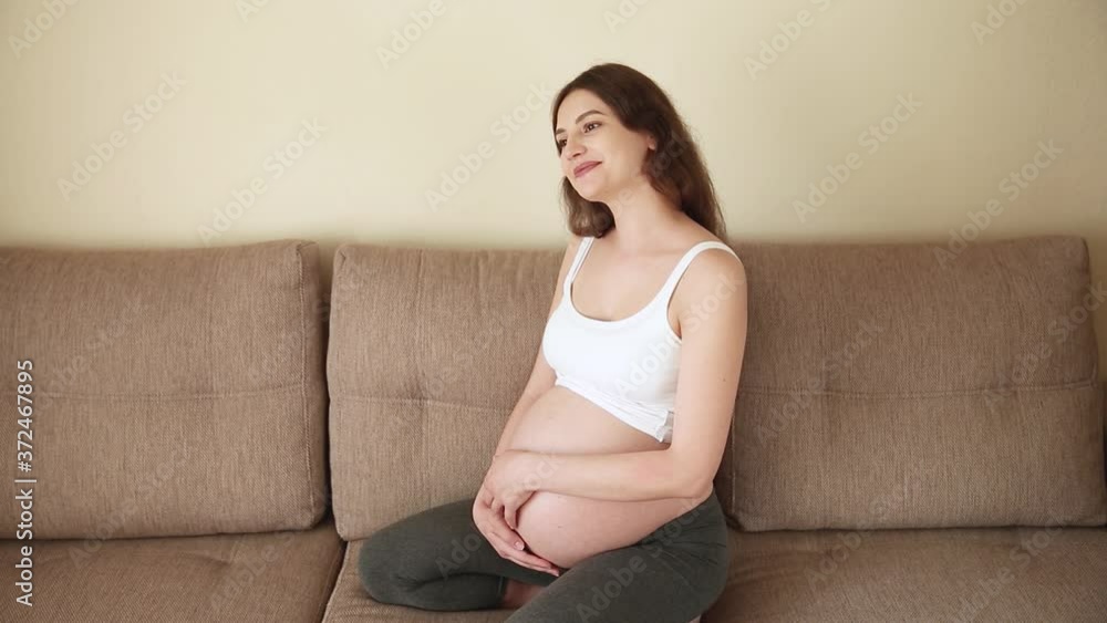 Portrait of caring mother strokes a naked pregnant tummy with two hands, on light room. A pregnant woman strokes a large belly in the sunny summer day Portrait of caring mother strokes a naked pregnant tummy with two hands, on light room. A pregnant woman strokes a large belly in the sunny summer day