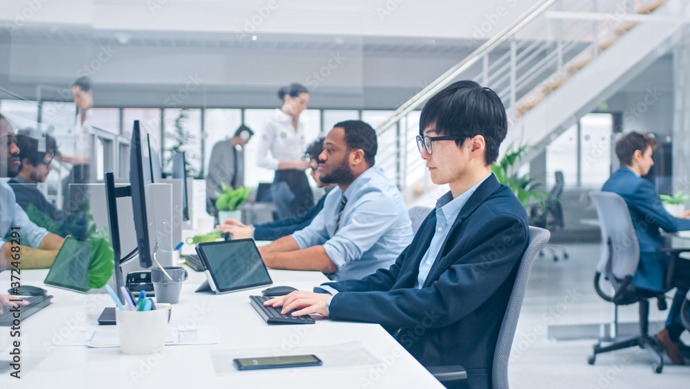 Shot of a Young Japanese Business Specialist Works on Desktop Computers. Diverse Team of Young and Motivated Businesspeople in Modern Open Office. Shot of a Young Japanese Business Specialist Works on Desktop Computers. Diverse Team of Young and Motivated Businesspeople in Modern Open Office.
