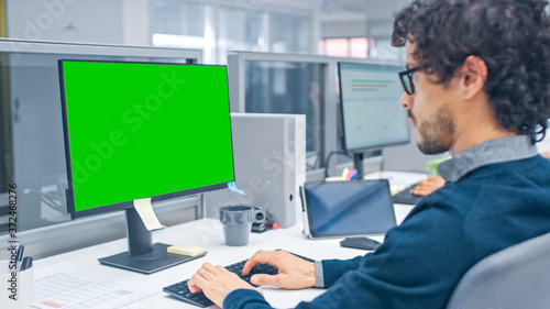 Young Handsome Manager with Curly Hair Works on a Desktop Computer with Green Screen Mock Up. Diverse and Motivated Business People Work on Computers in Modern Open Office.